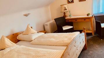 A bedroom with two beds, a desk, a chair, and a small table with a lamp.