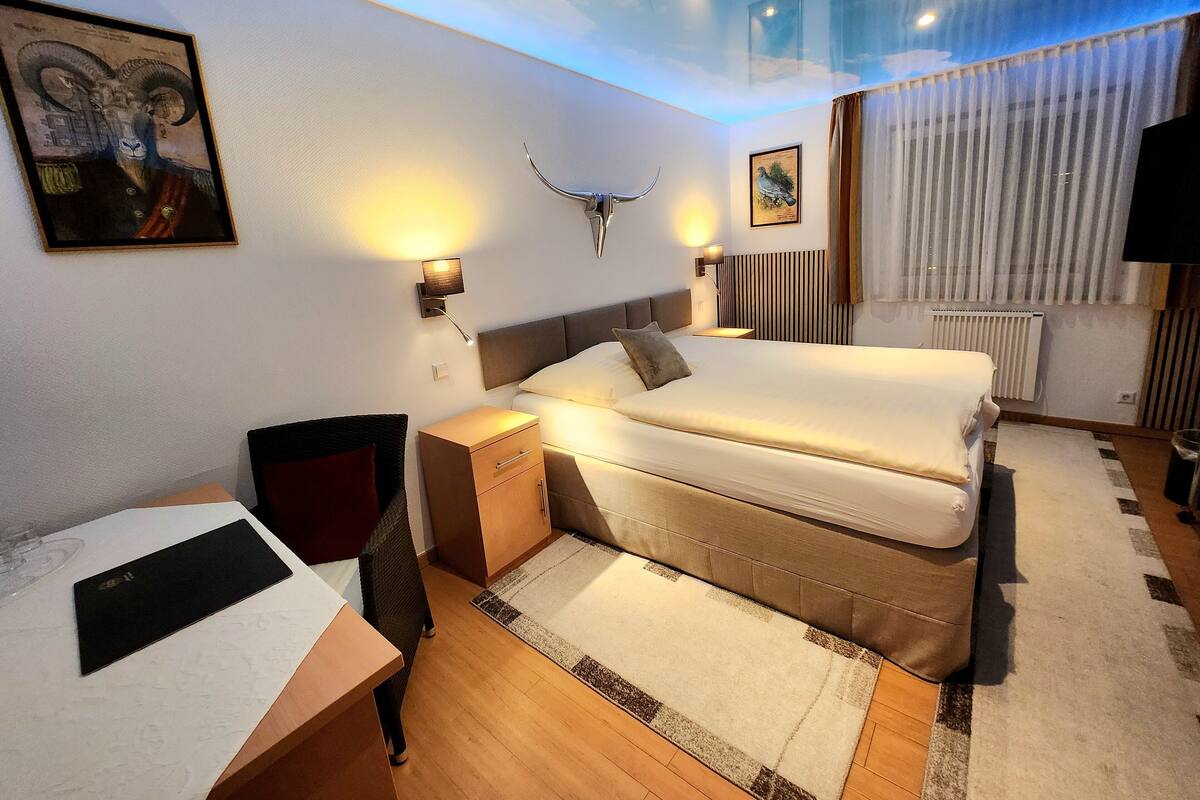 Een hotelkamer met een bed, nachtkastjes, een bureau, een stoel en kunstwerken aan de wanden.