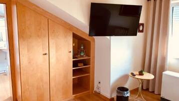 Een kamer met een houten garderobe, een wandtelevisie, een klein tafeltje met een stoel en een radiator.