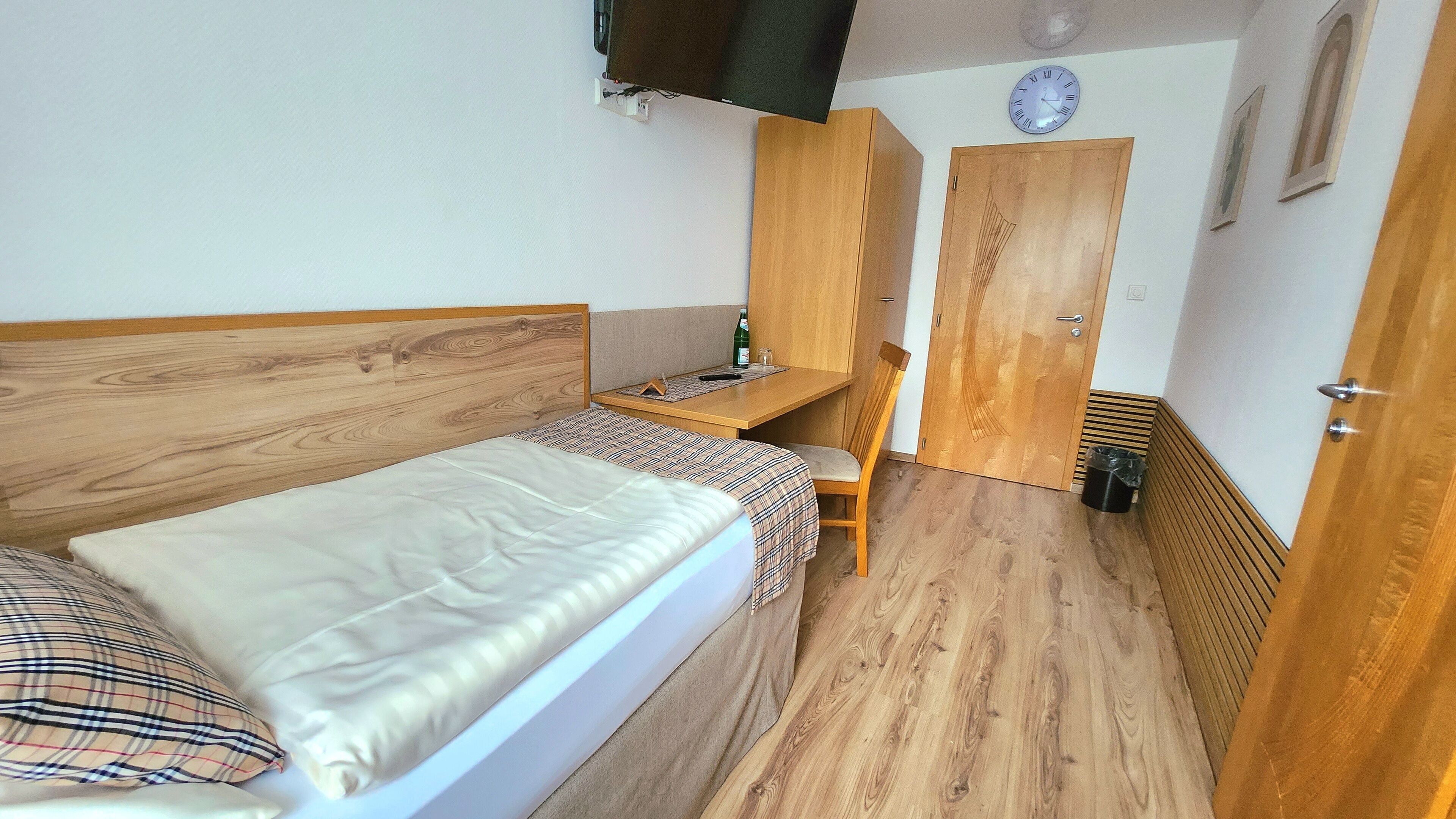 Une petite pièce, de taille modeste, comprenant un lit simple, un bureau en bois, une chaise et une armoire.