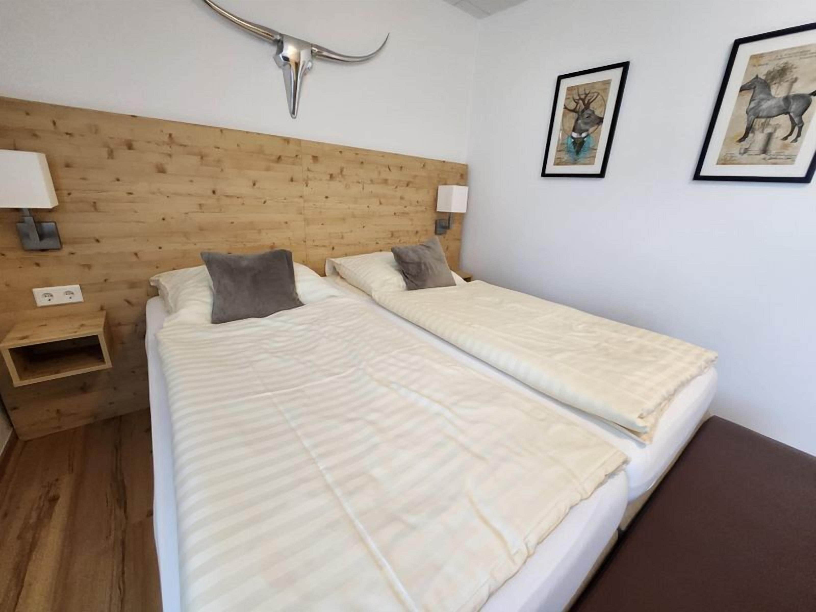 Une chambre avec deux lits, une tête de lit en bois, des lampes fixées au mur et deux tableaux encadrés.
