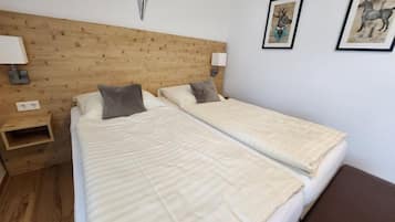 A room with two beds, wooden headboard, wall-mounted lights, and two framed pictures.