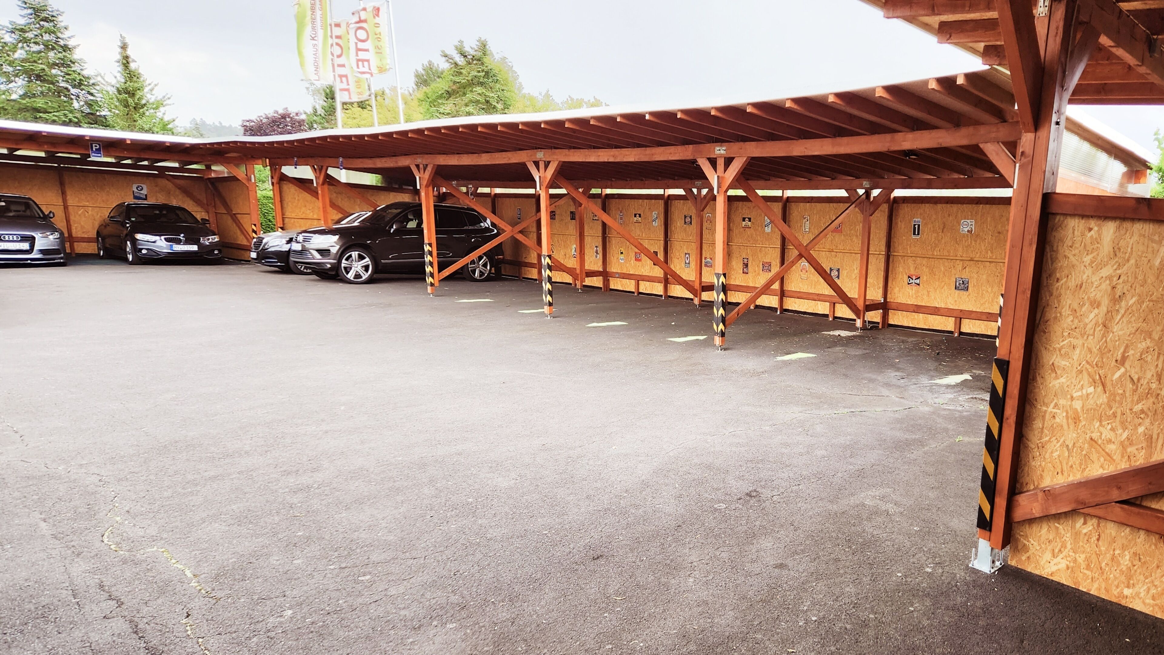 A covered parking area with multiple cars parked under a wooden structure.