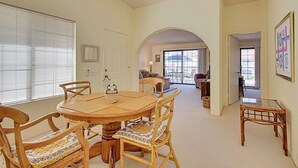 A dining area with a round wooden table and chairs, a ceiling fan, and a view through an arched doorway to a living room. - Villa Antonella (Palm Springs)