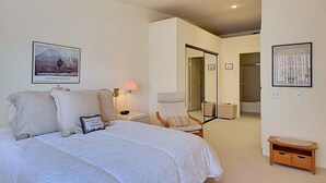 A bedroom with a large bed, a chair, a nightstand, and a lamp. There is a door leading to another room. - Villa Antonella (Palm Springs)