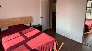 Une chambre à coucher avec un lit doté d’une tête de lit en bois, une petite table de chevet et une porte donnant sur une autre pièce.