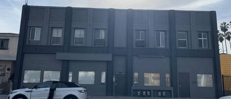 En bygning med flere etager, flad facade, store vinduer og en parkeringsplads med biler.