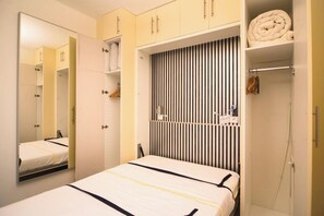 A bedroom with a bed, a wardrobe, a mirror, and a striped headboard.