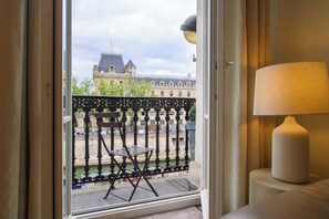 Ein Balkon mit Stuhl und Lampe, mit Blick auf ein Gebäude mit markantem Dach.