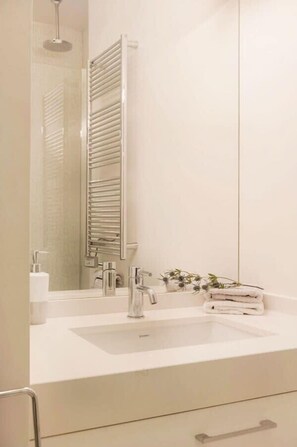 A modern bathroom with a large mirror, a white sink, and a towel rack.