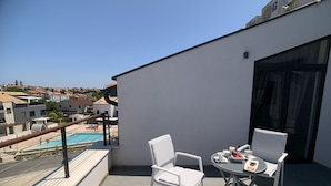 Ein Balkon mit zwei weißen Stühlen und einem kleinen Tisch, mit Blick auf einen Pool und eine Wohngegend.