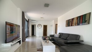 Ein modernes Wohnzimmer mit Flachbildfernseher, einem grauen Ecksofa, einem weißen Couchtisch und einem farbenfrohen Teppich.