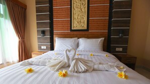 A hotel room with a large bed, neatly made pillows, and a decorative wall carving. - Kubu Willis (Legian)