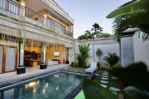 A modern building with a pool, outdoor seating, and greenery. - Kubu Willis (Legian)