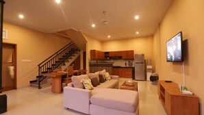 A spacious living area with a sofa, a wooden coffee table, and a television mounted on the wall. - Kubu Willis (Legian)