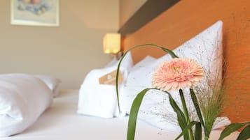 Un lit bien fait, avec du linge de lit blanc, une seule fleur rose et un élément décoratif mural.