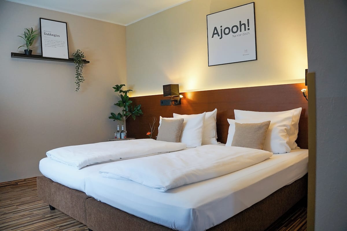 A double bed with white linens, a wooden headboard, and a framed sign on the wall.