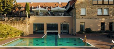 A swimming pool with a sun terrace, stone buildings, and a view of the surrounding area.