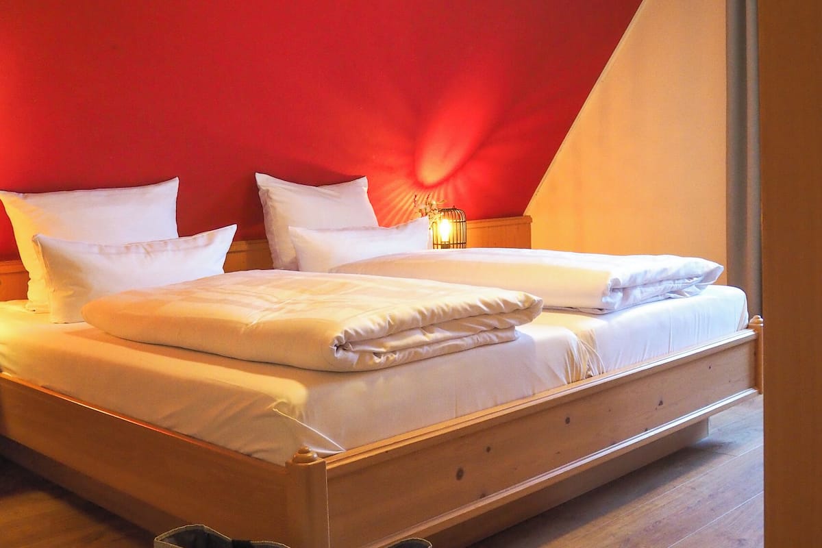 A bedroom with a wooden bed, white bedding, and a red accent wall.