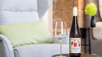 Una botella de vino y una copa vacía sobre una mesa redonda pequeña en una habitación con un sillón gris y un cojín verde.