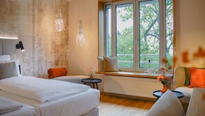 A modern hotel room with a large bed, a seating area with a view of trees, and a window with a view of the outdoors. - Leinsweiler Hof (Leinsweiler)