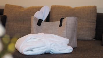 A neatly folded white bathrobe on a brown couch with a woven bag containing slippers.