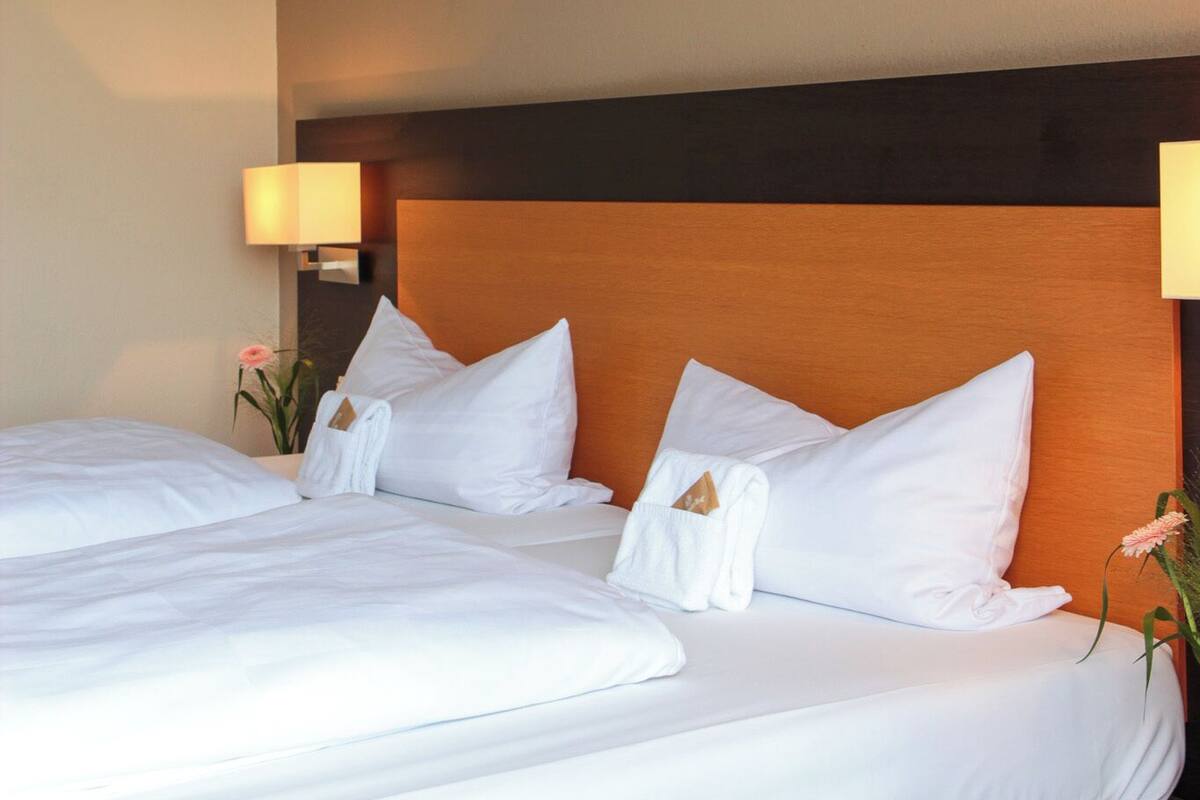 A hotel room with two beds, a wooden headboard, bedside lamps, and a small table.