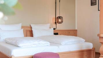 Una cama bien hecha con sábanas y almohadas blancas, cabecera de madera y una lámpara colgante.