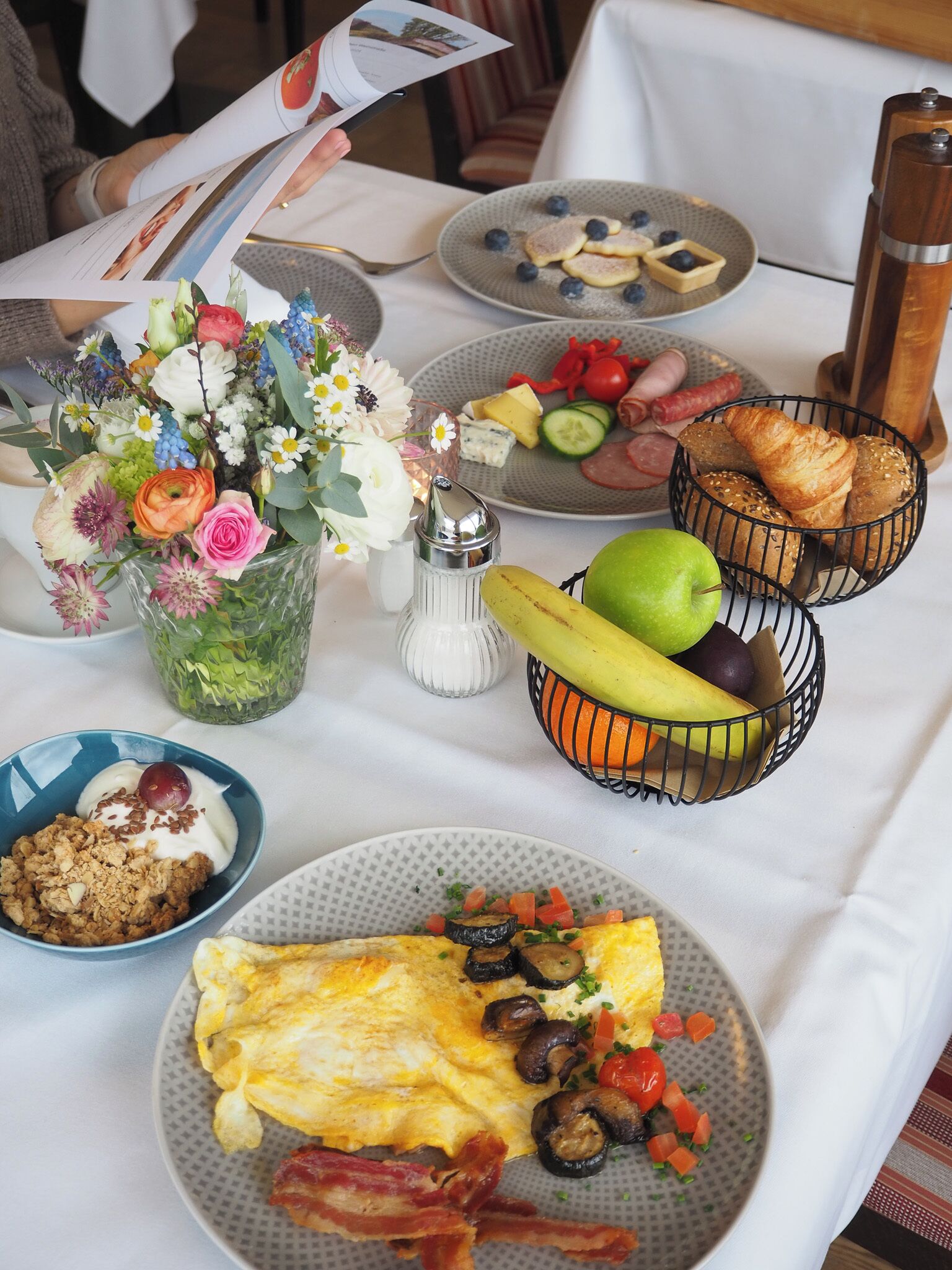 A breakfast table with a variety of food items, including eggs, bacon, toast, and a fruit basket.