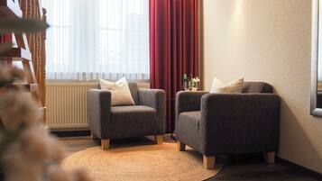 A cozy living room with two armchairs, a woven rug, a radiator, and a window with sheer curtains.