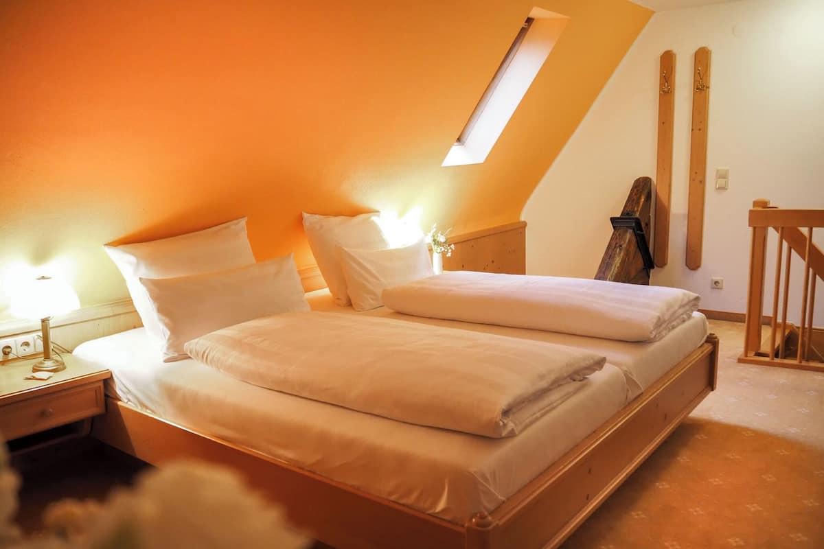 A bedroom with a sloped ceiling, a bed with white linens, a nightstand, and a wooden headboard.