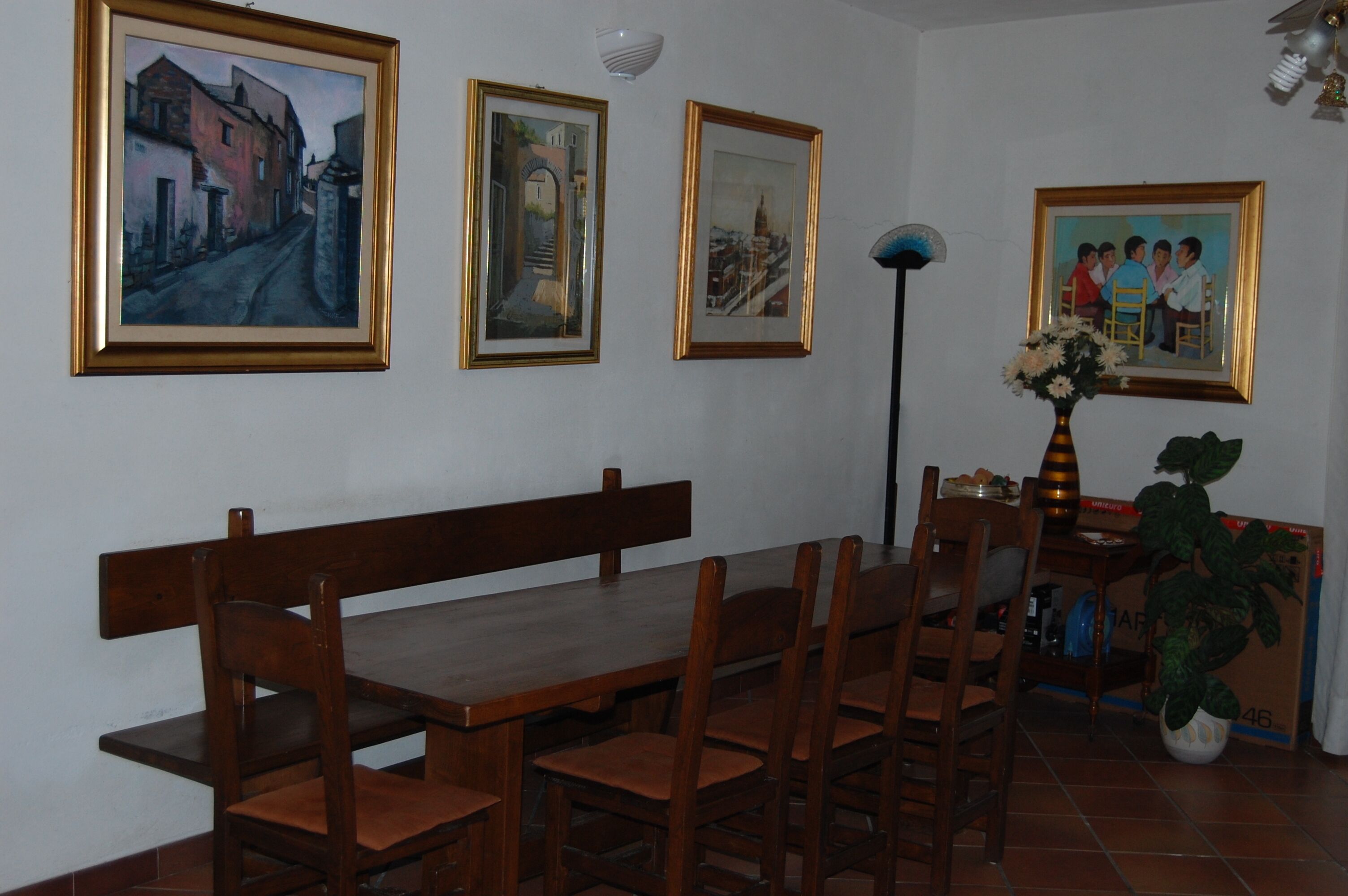 Un'area pranzo con tavolo e sedie in legno, quadri appesi alla parete e un tavolino con un vaso di fiori.