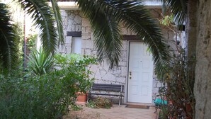 A stone building with a white door, a bench, and potted plants. - Isolated villa surrounded by greenery a stone's throw from Olbia (Olbia)