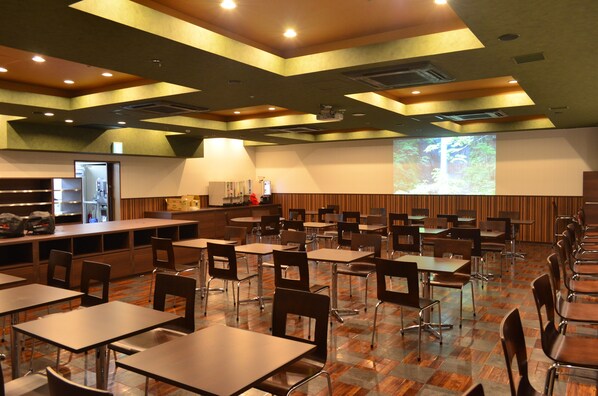 A spacious restaurant with multiple tables and chairs, a bar area, and a large screen displaying a nature scene.