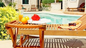 A wooden lounge chair by a pool with a drink tray, a towel, and sunglasses. - Apartments Salu (Medulin)