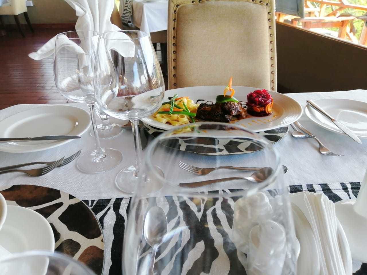 A dining table set with plates, cutlery, and wine glasses, with a zebra-patterned table runner.