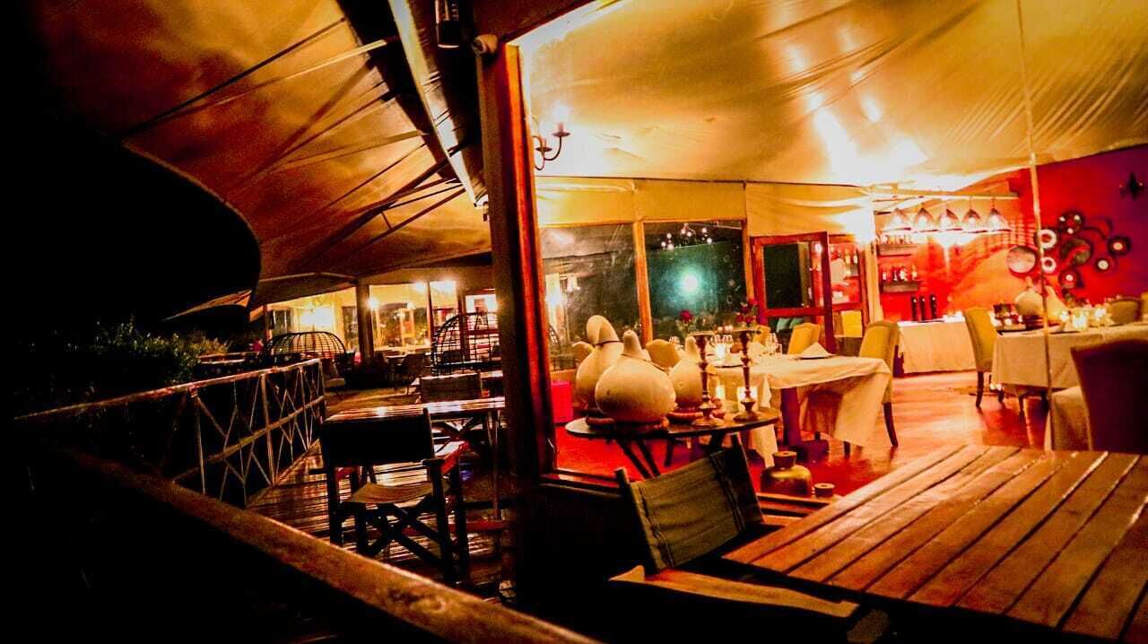 Un espace de restauration en plein air avec des tables et des chaises en bois, un coin salon abrité et une vue sur l’intérieur du restaurant.
