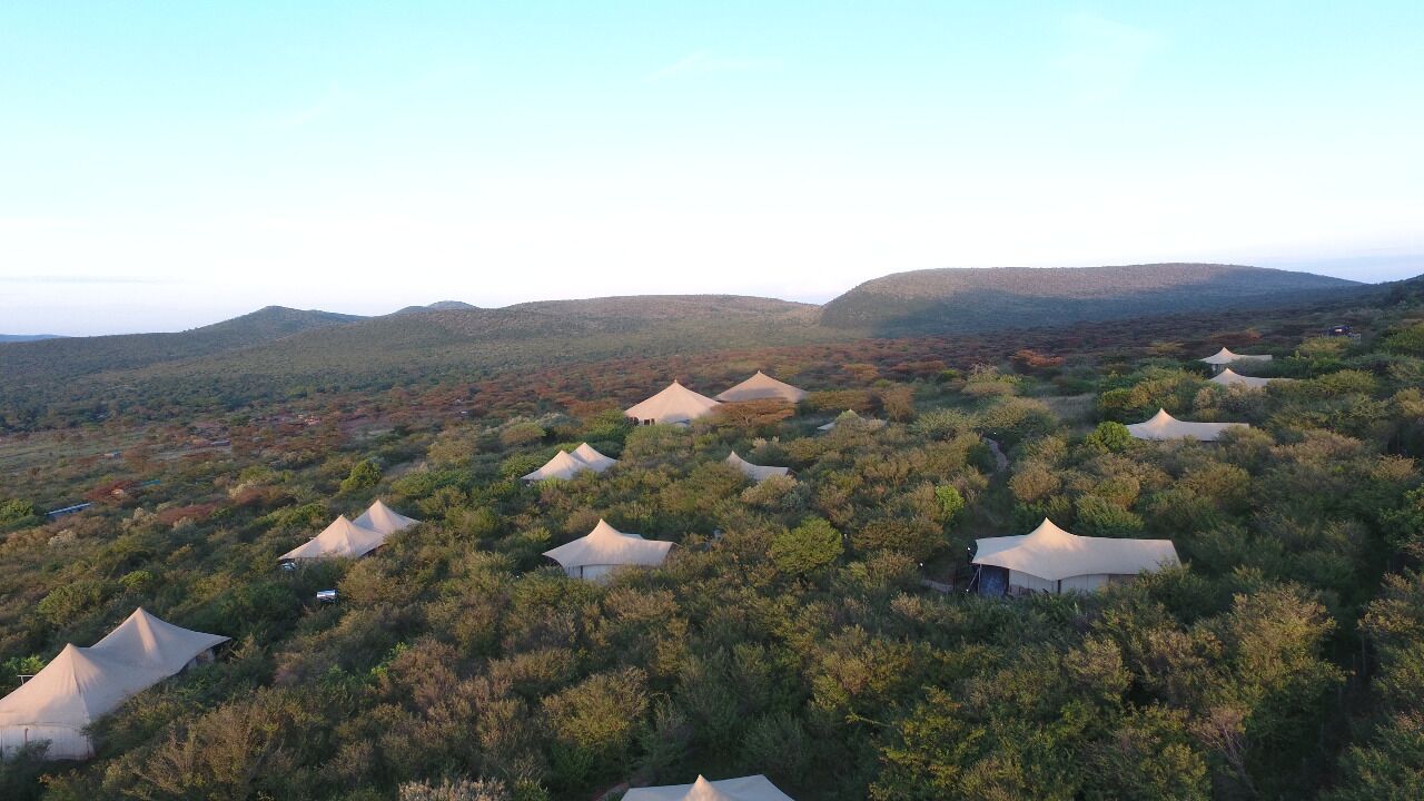 A series of tents set in a natural landscape with hills in the background.