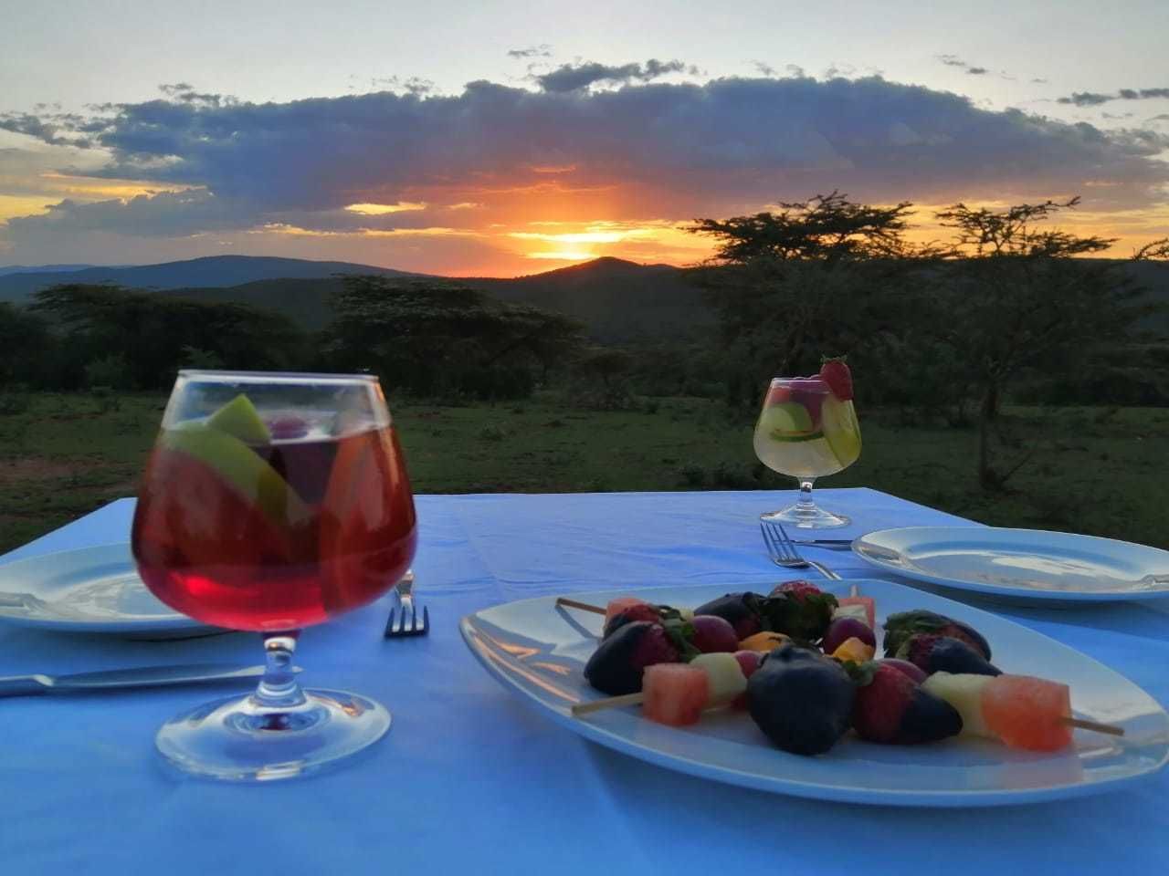 Een gedekte tafel met een diner en uitzicht op de zonsondergang, een glas rode wijn en een dessertglas.