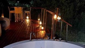 A hot tub with rose petals floating on the water, surrounded by a wooden deck and outdoor furniture.