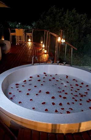 A hot tub with rose petals floating on the water, surrounded by a wooden deck and outdoor furniture. - Emayian Luxury Camp (Maasai Mara)