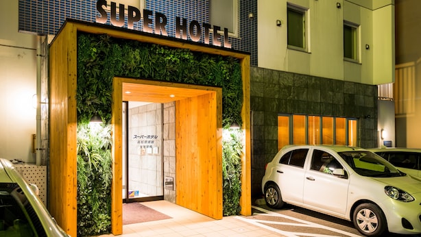 The entrance to a hotel with a sign reading "Super Hotel" and a car parked in front. - Super Hotel Takamatsu Kinenkan (Takamatsu)