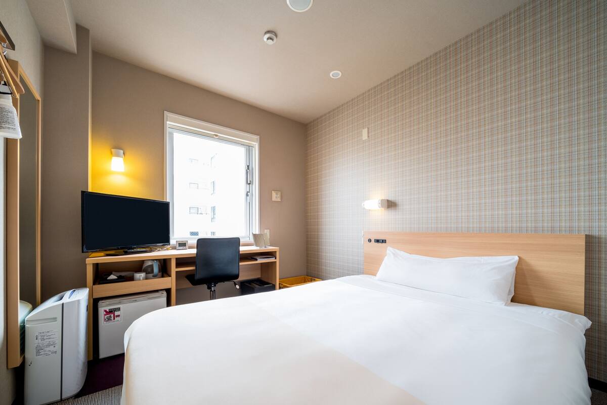 A hotel room with a bed, a desk with a computer, a television, and a window.