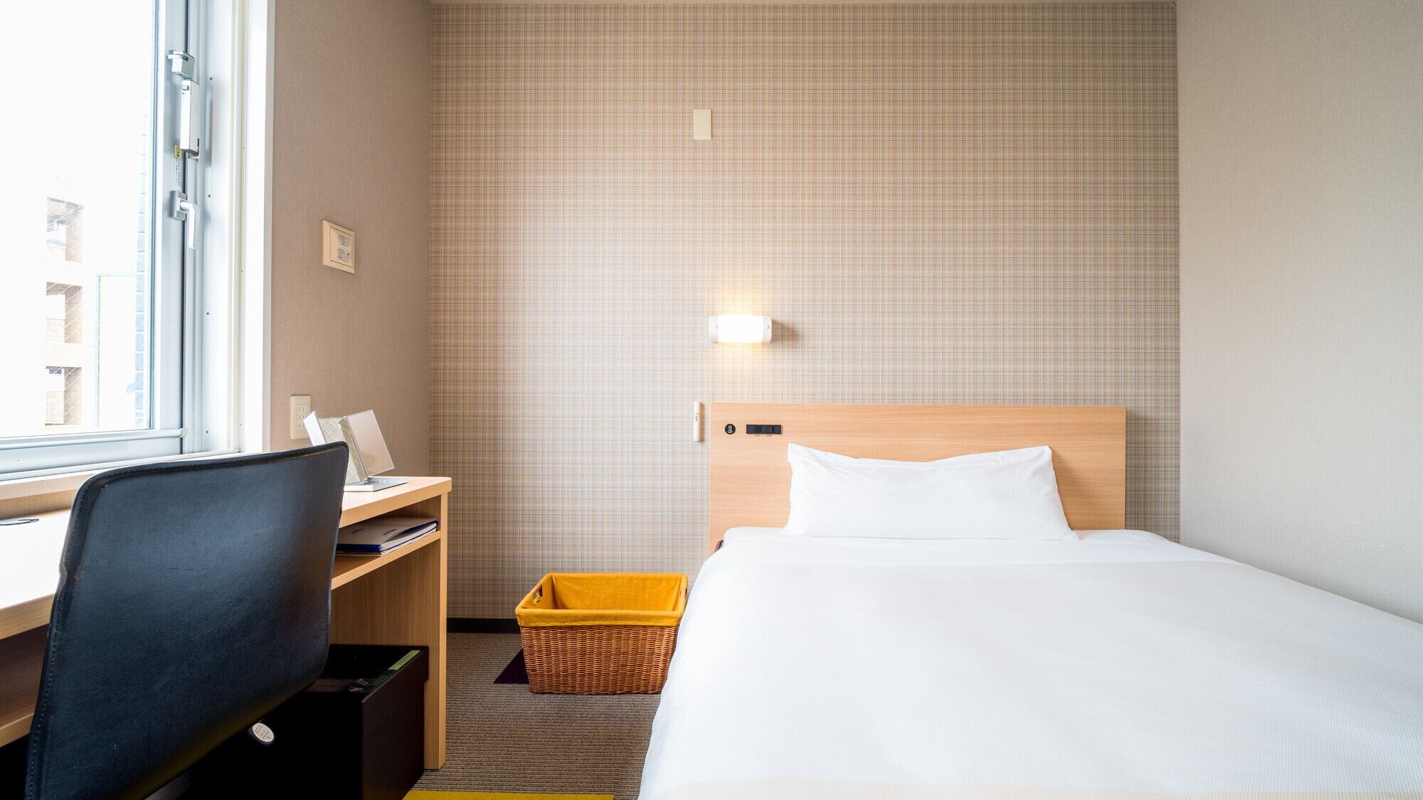 Quarto de hotel com cama, escrivaninha, cadeira e janela.
