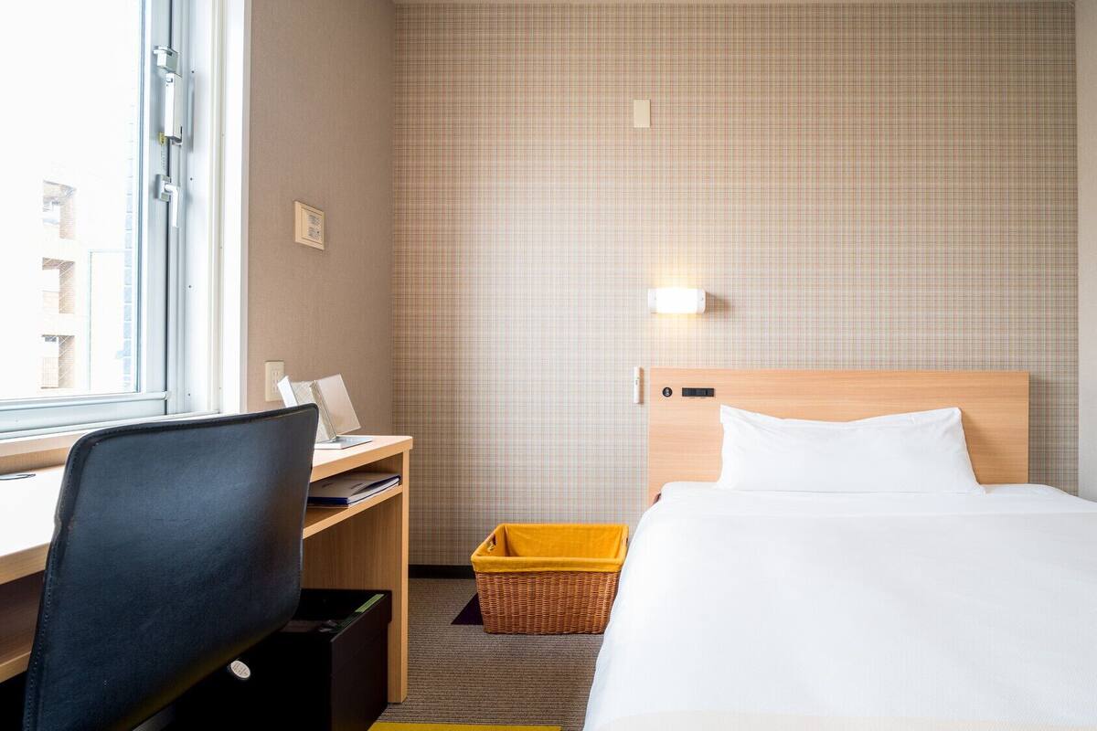 A hotel room with a bed, desk, chair, and a window.
