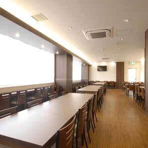 A conference room with long tables and chairs, a flat-screen TV mounted on the wall, and a large window providing natural light. - Ab Hotel Toyohashi (Toyohashi)