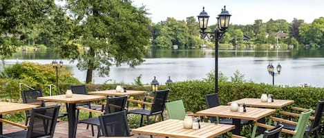 Outdoor tables and chairs by a lake with a view of houses in the background.