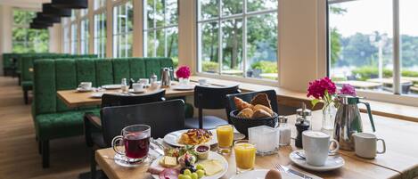 A breakfast setting with a table set for two, including plates of food, drinks, and a coffee pot.
