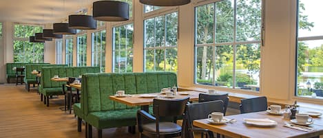 Un restaurante con asientos tapizados en verde, mesas de madera y lámparas colgantes.