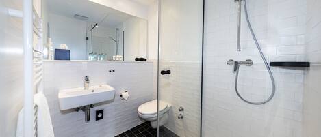 A modern bathroom with a glass-enclosed shower, a white sink, and a toilet.